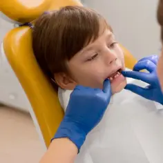 Chłopiec u dentysty, który bada jego zęby. Lekarz w niebieskich rękawiczkach sprawdza, czy nie ma zapalenia dziąseł u dziecka.