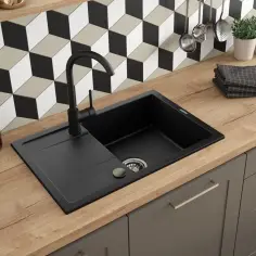 Czarny zlew granitowy z baterią na drewnianym blacie, w tle geometryczna mozaika.