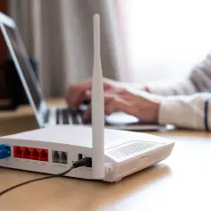 Router z antenkami i kablami, gotowy do podłączenia internetu na kartę. W tle osoba pracuje na laptopie.