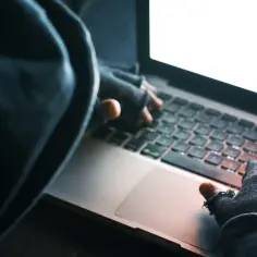 Osoba w kapturze i rękawiczkach pisze na laptopie. To może być początek kradzieży tożsamości.