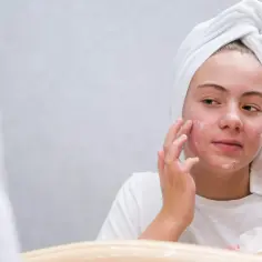 Dziewczyna z ręcznikiem na głowie aplikuje maść z witaminą A na twarz, licząc na jej pozytywne efekty w walce z niedoskonałościami.