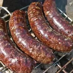 Cztery soczyste kiełbaski z grilla pieką się na ruszcie, uwalniając apetyczny aromat.
