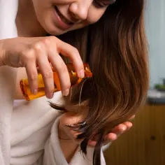 Kobieta w szlafroku aplikuje olejek na końcówki włosów, by je nawilżyć.