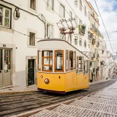 Żółty tramwaj zjeżdża po brukowanej ulicy w Lizbonie, stolicy nad estuarium Tagu.