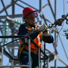 Elektryk w kasku i kamizelce pracujący na wysokości. Zastanawiasz się, ile zarabia elektryk? To praca wymagająca i odpowiedzialna.