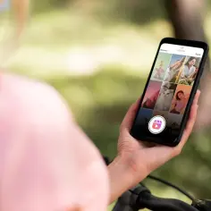 Osoba trzyma telefon z aplikacją Instagram, przeglądając zdjęcia. Widoczny jest przycisk Reels, sugerujący, jak zrobic rolke ze zdjec.