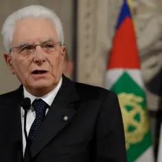 Sergio Mattarella, prezydent Włoch, przemawia na tle flag.