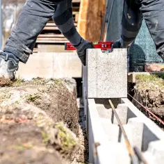 Budowniczy układa bloczek betonowy, sprawdzając poziom. Powstaje ściana z bloczka betonowego.
