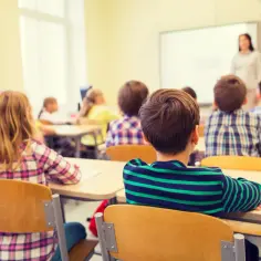 Dzieci siedzą w klasie, słuchając nauczycielki. Tematem lekcji jest religia w szkole, a uczniowie uważnie obserwują tablicę.