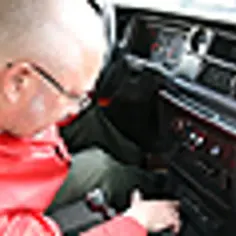 Mężczyzna w czerwonej kurtce pochyla się nad deską rozdzielczą, szukając przyczyny, dlaczego radio nie łapie fal w samochodzie.