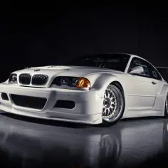Białe BMW M3 GTR w wyścigowej odsłonie, z szerokimi błotnikami i spojlerem, gotowe do akcji na torze.