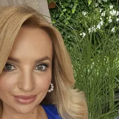 Uśmiechnięta Ilona Januszewska, której wiek dodaje jej uroku, pozuje na tle zieleni.