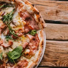 Pyszna pizza carbonara z chrupiącym boczkiem, rukolą i cebulą na drewnianym stole.