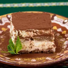 Pyszny włoski deser tiramisu, posypany kakao, na ozdobnym talerzu z listkiem mięty.
