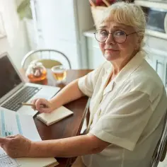 Kobieta z okularami analizuje dokumenty, planując emeryturę za 4 dzieci. Na stole laptop, herbata i notatnik.