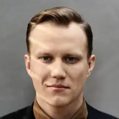 Mężczyzna o niebieskich oczach i zaczesanych włosach, ubrany w ciemną marynarkę i brązową koszulę. Jego twarz zdaje się opowiadać historię, jakby przetrwał wiek mrozu.