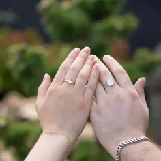 Dłonie z wyeksponowanymi sygnetami damskimi srebrnymi. Jeden z nich ozdobiony literą "J", drugi subtelnym kamieniem.
