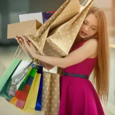Kobieta z telefonem przy uchu, przytłoczona zakupami. Czy to uzależnienie od zakupów?