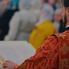 Duchowny w czerwonej szacie z haftem czyta z księgi podczas nabożeństwa.