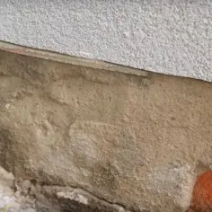 Fragment ściany z widocznym pęknięciem, przygotowanym do iniekcji. Widać warstwę tynku i ceglane podłoże.