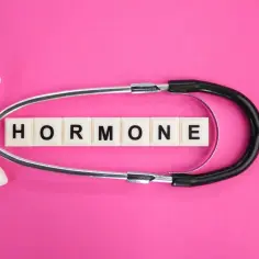 Stetoskop i litery tworzące słowo "HORMONE" na różowym tle. Może to symbolizować problemy z hormonami, np. niski progesteron w ciąży objawy.