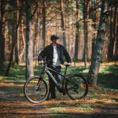Mężczyzna w kasku z rowerem w lesie, gotowy do odkrywania tras rowerowych w Łebie.