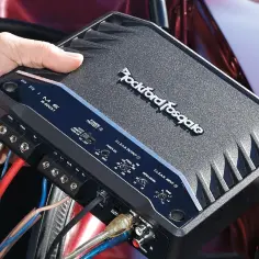 Podłączanie wzmacniacza samochodowego Rockford Fosgate. Czerwony kabel to plus, a czarny to minus dla głośników.