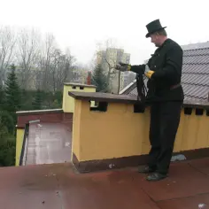 Kominiarz w cylindrze na dachu trzyma linę do czyszczenia komina.