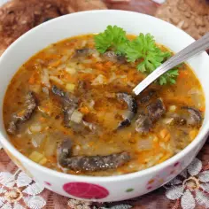 Aromaticzne flaczki z kani, bogate w kawałki grzybów i warzyw, podane w białej miseczce z natką pietruszki.