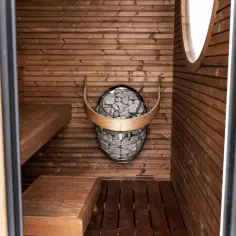 Wnętrze domowej sauny z drewnianymi ławami i kamiennym piecem.