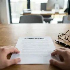 Dłoń na dokumencie "Rozwiązanie umowy", obok długopis i okulary. To moment, gdy zastanawiasz się, jak się pisze wypowiedzenie z pracy.