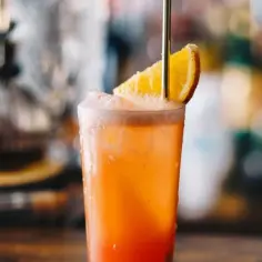 Orzeźwiający drink Campari Orange z plasterkiem pomarańczy i metalową słomką, idealny na letnie popołudnie.