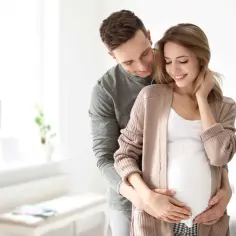 Szczęśliwy mąż obejmuje żonę w ciąży, okazując troskę i miłość. To piękny obraz wsparcia i oczekiwania na dziecko, symbolizujący opiekę na żonę po porodzie.