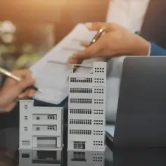 Dwie makiety budynków, dokumenty i laptop. Rozmowa o przyszłości i dziedziczeniu.