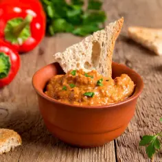 Pomarańczowy dip w glinianej miseczce z grzankami, paprykami i natką pietruszki na drewnianym tle.