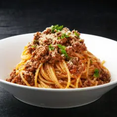 Pyszny makaron z mięsem mielonym, posypany parmezanem i natką pietruszki, podany w białej misce.