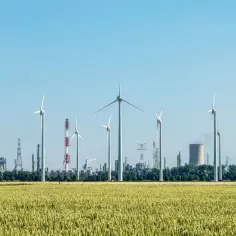 Wiatraki i przemysłowa infrastruktura na horyzoncie symbolizują elektryfikację i dążenie do zrównoważonej energii.