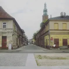 Ulica w Radomiu, z charakterystyczną wieżą kościelną w oddali. Stare kamienice po obu stronach ulicy, brukowana nawierzchnia.
