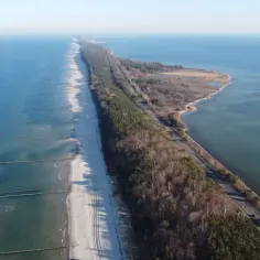 Długa, piaszczysta plaża z falochronami na Mierzei Helskiej, otoczona lasem i wodą. Idealne miejsce na kąpielisko.