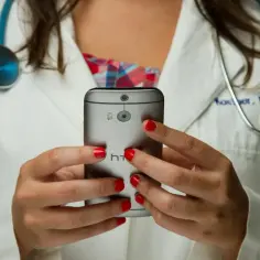 Lekarka w białym kitlu z czerwonymi paznokciami trzyma telefon. Czy pracodawca widzi kod choroby na ekranie?