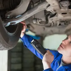 Mechanik z latarką bada podwozie auta, by uniknąć kary za spóźniony przegląd.