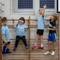 Cztery dzieci w strojach sportowych wykonują ćwiczenia ruchowe dla dzieci na drabinkach gimnastycznych.