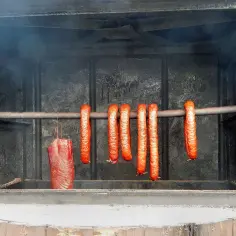 Wędzone kiełbaski i kawałek mięsa wiszą w wędzarni. Kluczowe jest, jaka temperatura mięsa w środku podczas wędzenia, by było idealne.