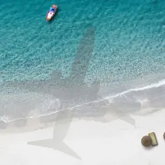 Cień samolotu nad turkusową wodą i piaszczystą plażą. Zastanawiasz się, ile godzin leci się na Zanzibar z Polski?