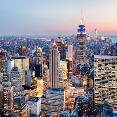 Widok na rozświetlony Nowy Jork o zmierzchu, z Empire State Building w centrum. Zastanawiasz się, ile kosztuje lot do USA?