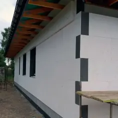 Ocieplenie domu styropianem w trakcie budowy. Białe płyty styropianowe pokrywają ściany, tworząc solidną izolację.