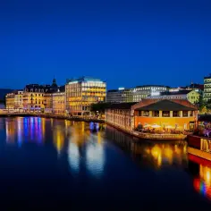Wieczorem nad rzeką w Genewie, gdzie leży to piękne miasto, widać oświetlone budynki i fontannę Jet d'Eau.