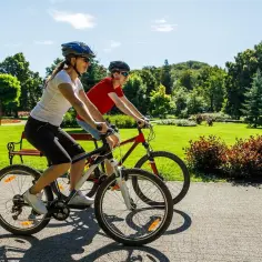 Dwie osoby na rowerach cieszą się piękną pogodą w parku. To pokazuje, co daje jazda na rowerze: aktywność, relaks i kontakt z naturą.