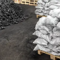 Kupa węgla obok worków z węglem na paletach.