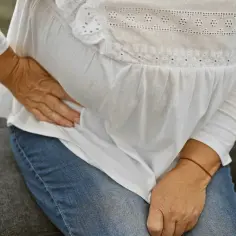 Kobieta siedząca na kanapie trzyma się za bolące biodro.